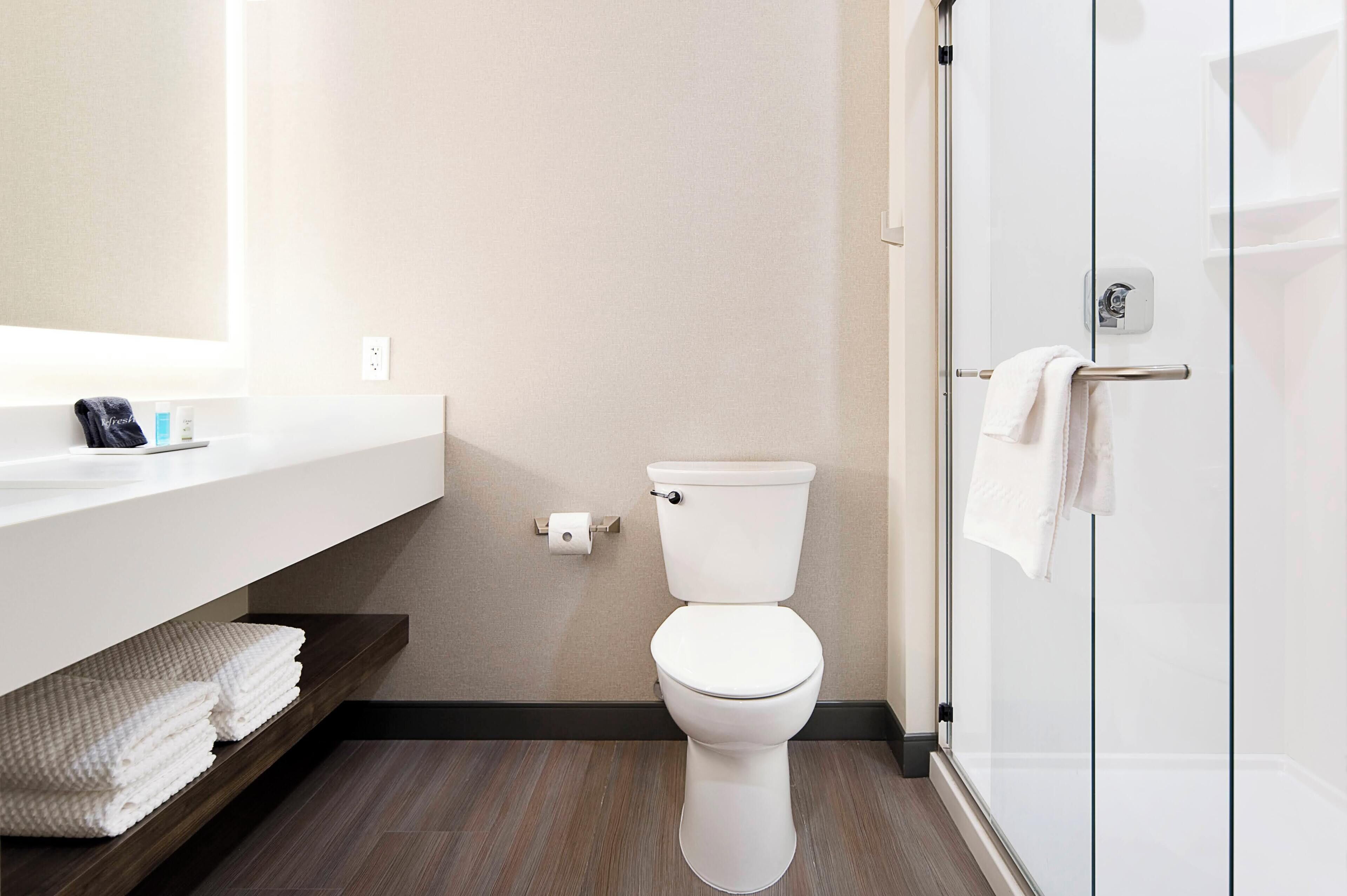 Une salle de bain moderne avec des toilettes, une douche à parois de verre et un meuble-lavabo blanc avec des serviettes.