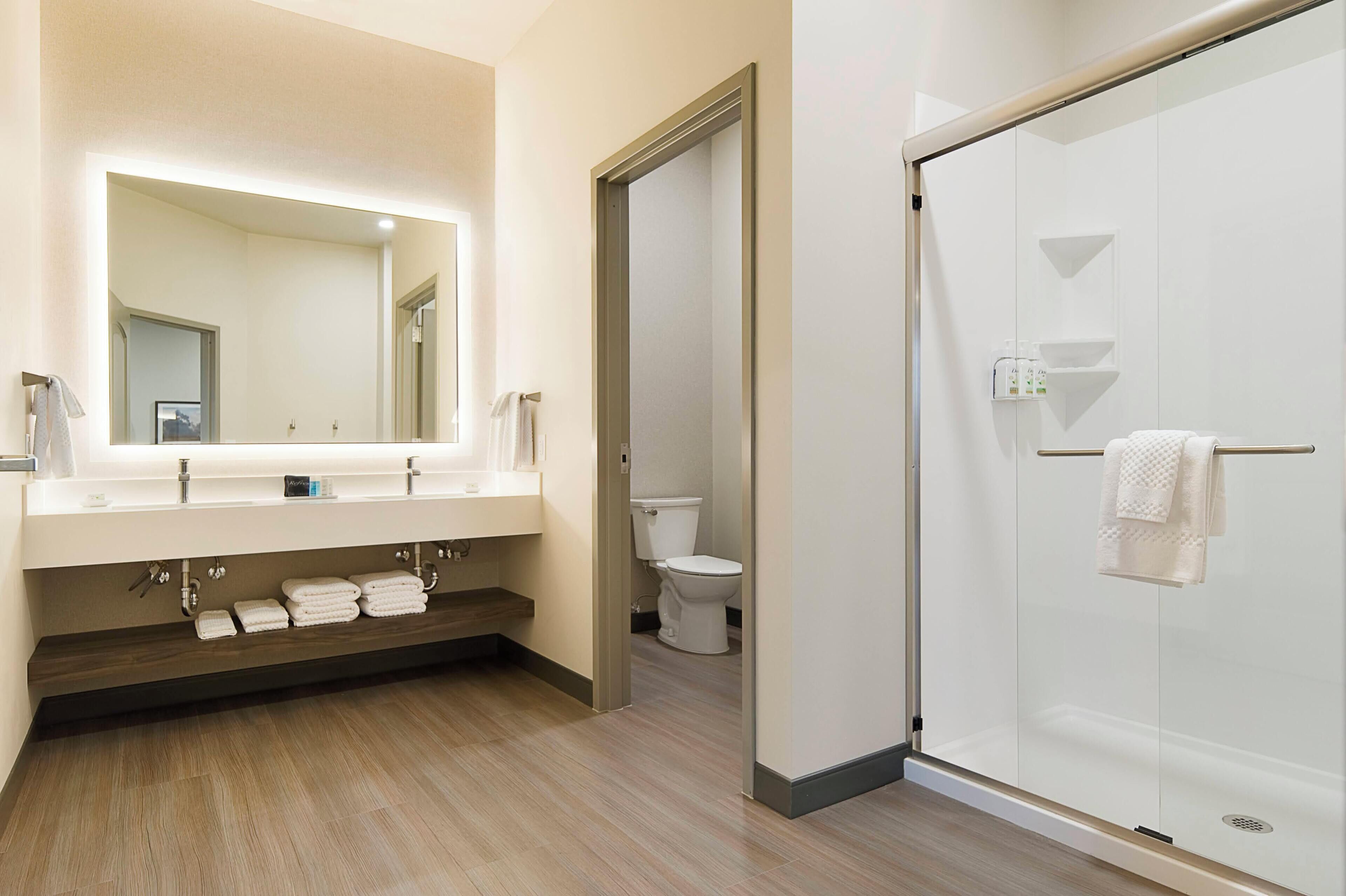 A modern bathroom with a large mirror, a glass-enclosed shower, and a toilet.