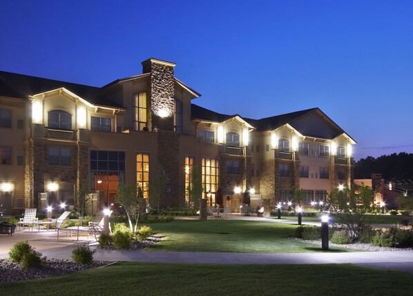 Un hotel grande de varios pisos con fachada de piedra, múltiples balcones y zonas de estar exteriores bien iluminadas.