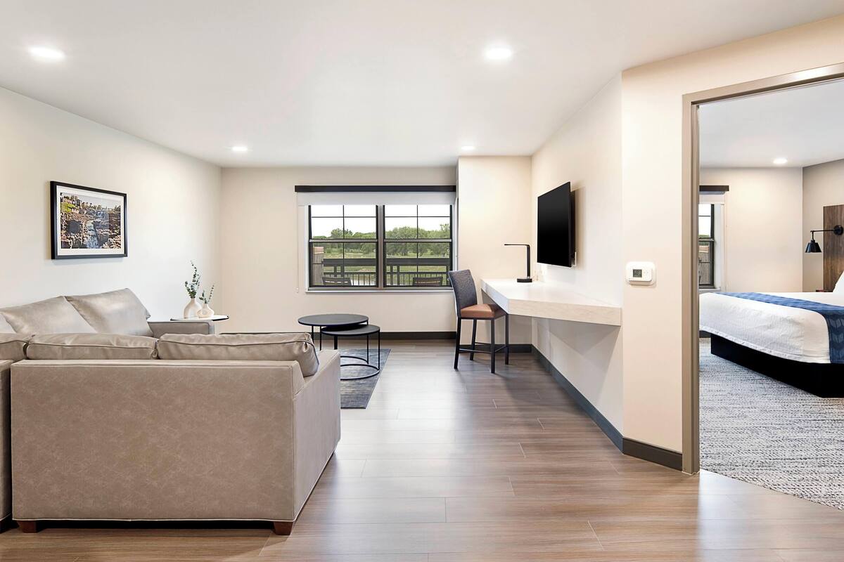 Une chambre d’hôtel moderne équipée d’un canapé, d’un bureau, d’une chaise, d’un lit, d’une télévision et d’une grande fenêtre.