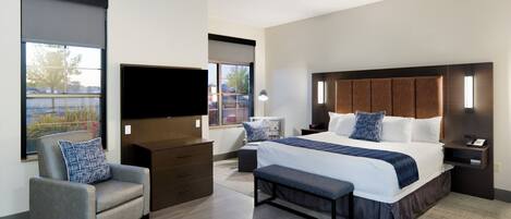 A modern hotel room with a large bed, a flat-screen TV, a desk, and a chair.