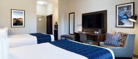 Quarto de hotel com duas camas, uma escrivaninha, uma televisão e um sofá.