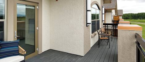 A covered deck with a bench and chairs, a glass door, and a view of the landscape.