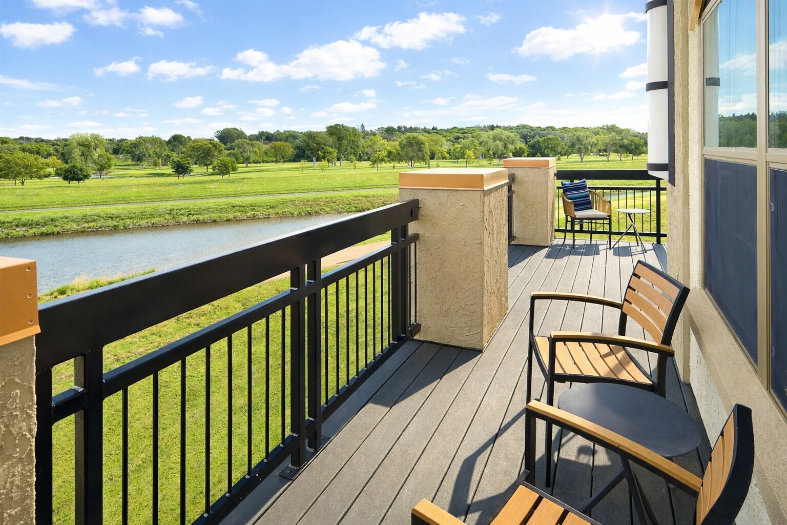 Terraza con vistas a un río y follaje, sillas de madera y una mesa.