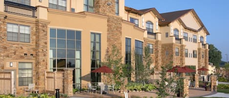 A multi-story building with a stone facade, large windows, and outdoor seating areas.