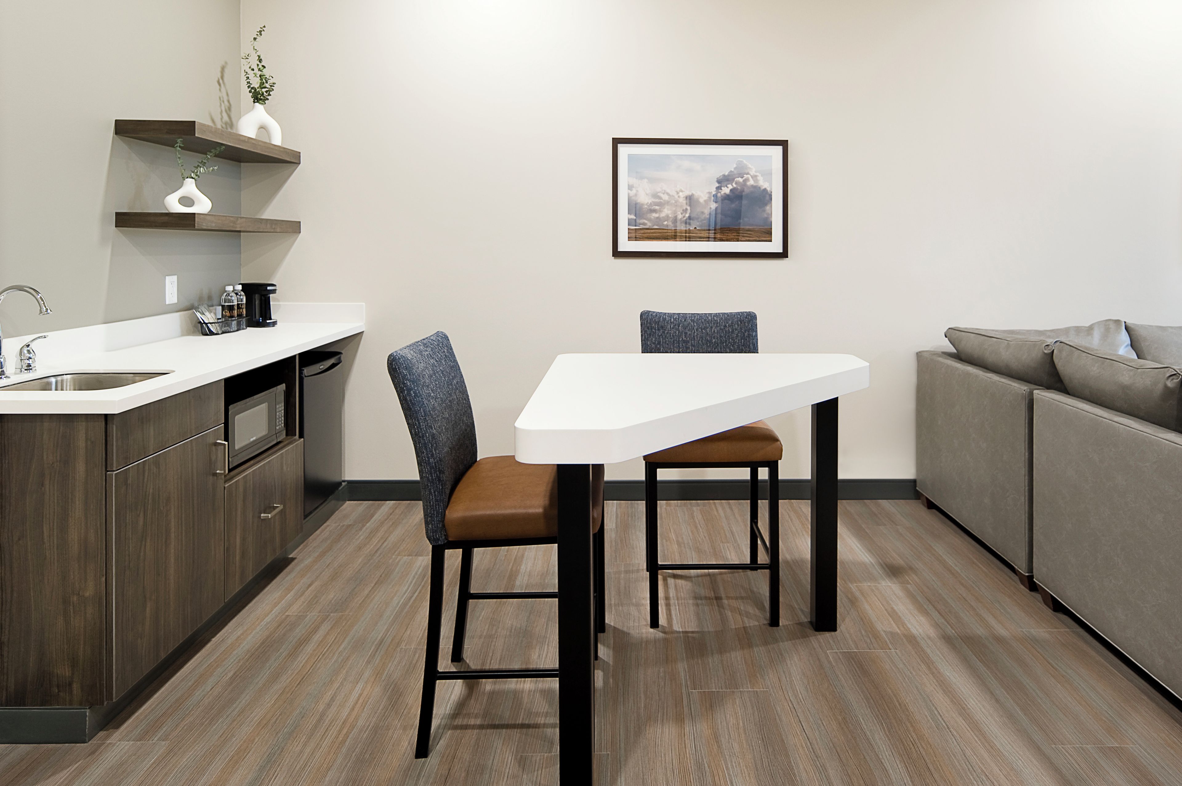 A modern kitchen with a white countertop, dark wood cabinets, a gray sofa, and a framed picture on the wall.