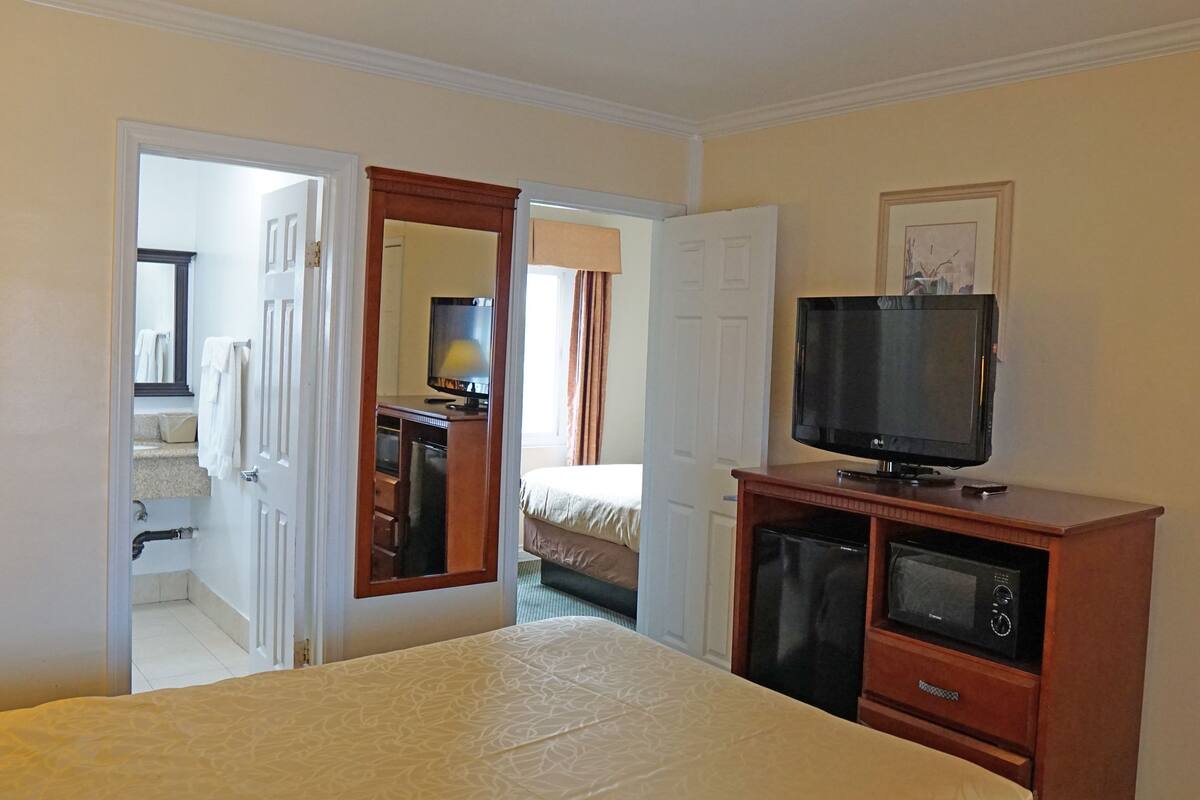 Habitación de hotel con cama, televisor sobre un soporte de madera, microondas y baño visible a través de una puerta abierta.