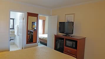 Habitación de hotel con cama, televisor sobre un soporte de madera, microondas y baño visible a través de una puerta abierta.