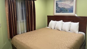 A hotel room with a large bed, a headboard, a window with curtains, and a framed picture on the wall.