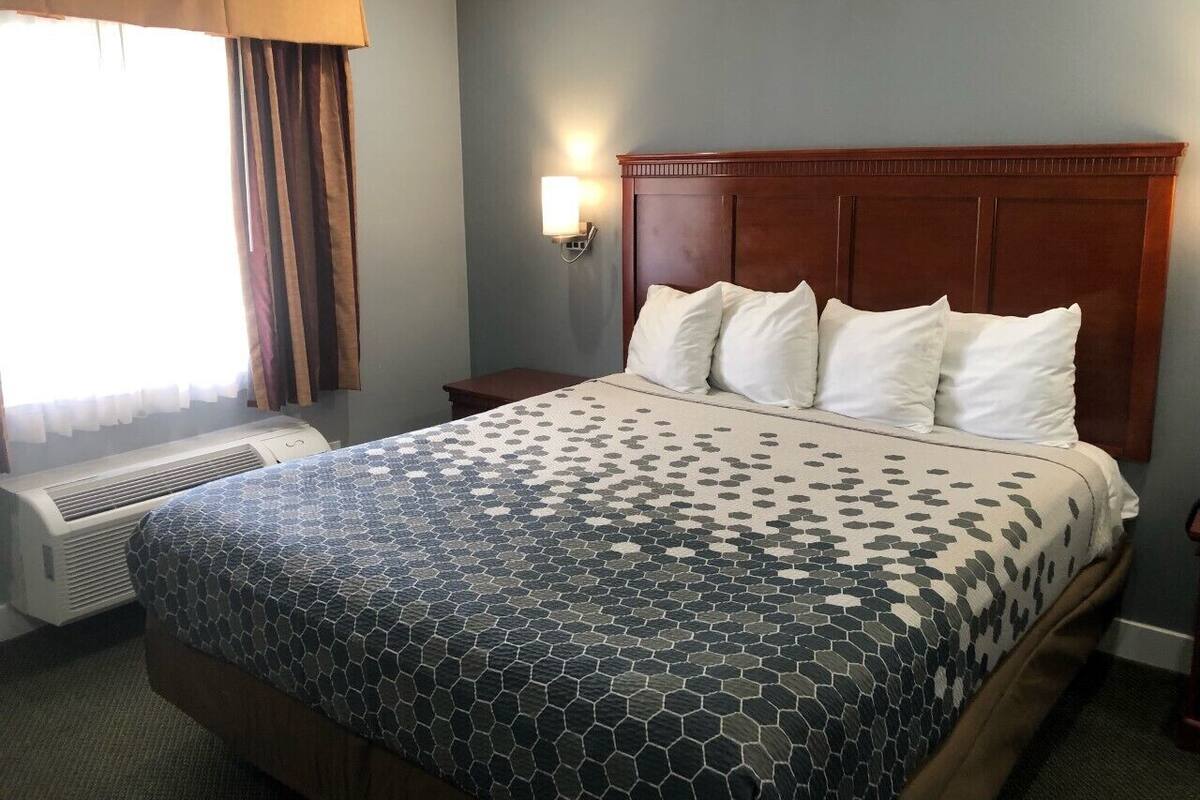 Habitación de hotel con una cama grande, una mesita de noche, una lámpara de pared y un equipo de aire acondicionado.