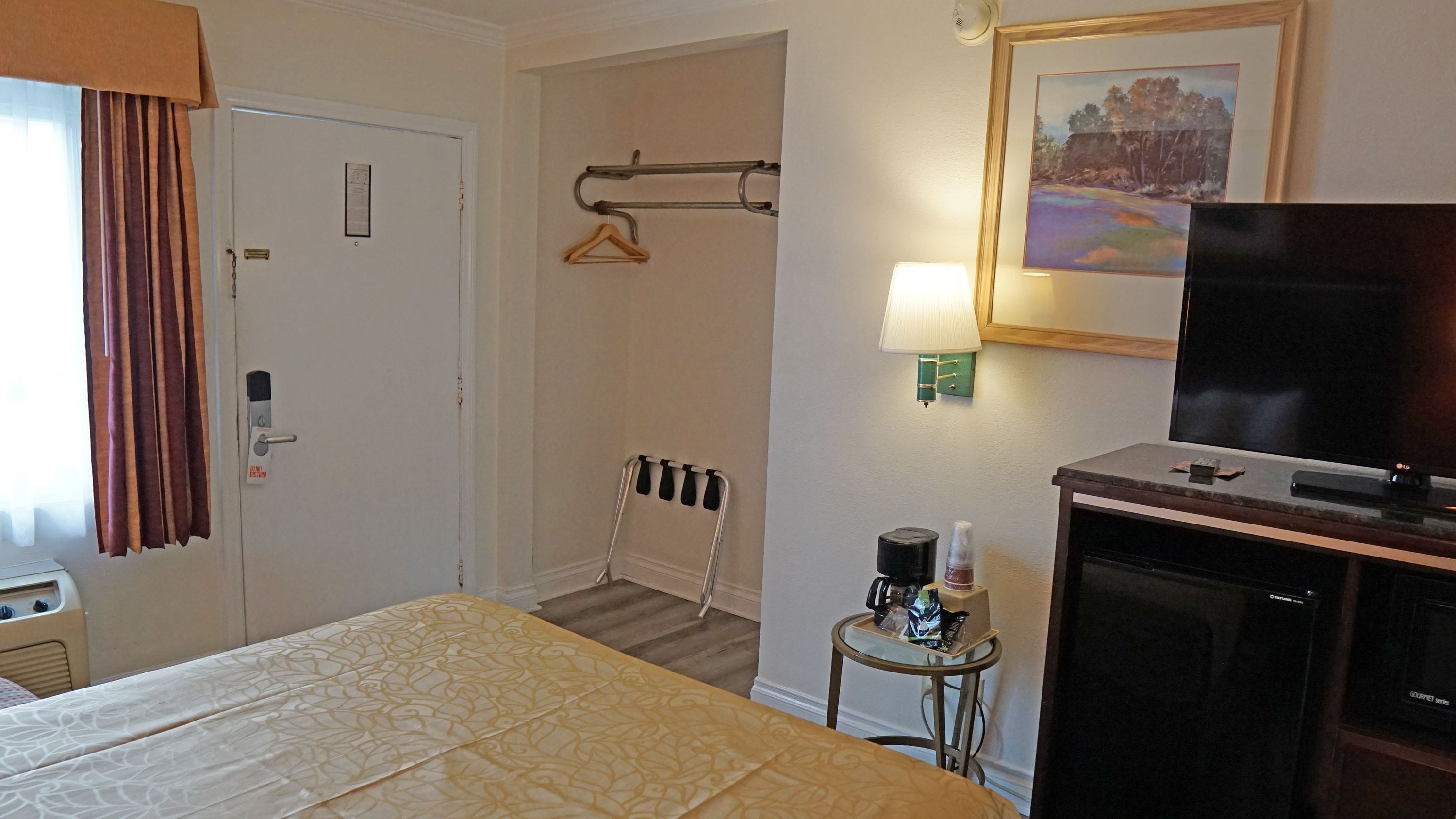 Habitación de hotel con cama, televisión, una mesita con cafetera y un cuadro en la pared.