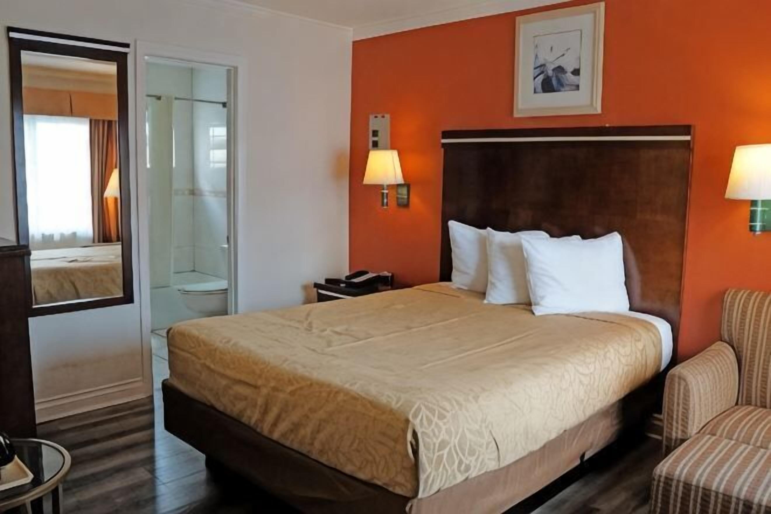 A hotel room with a large bed, two bedside lamps, a headboard, a chair, and a mirror.