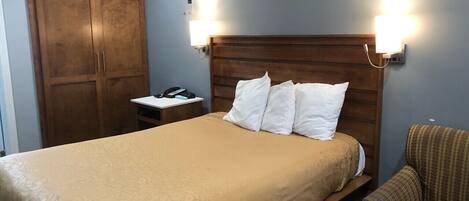 A hotel room with a bed, a nightstand, a chair, and a wardrobe.