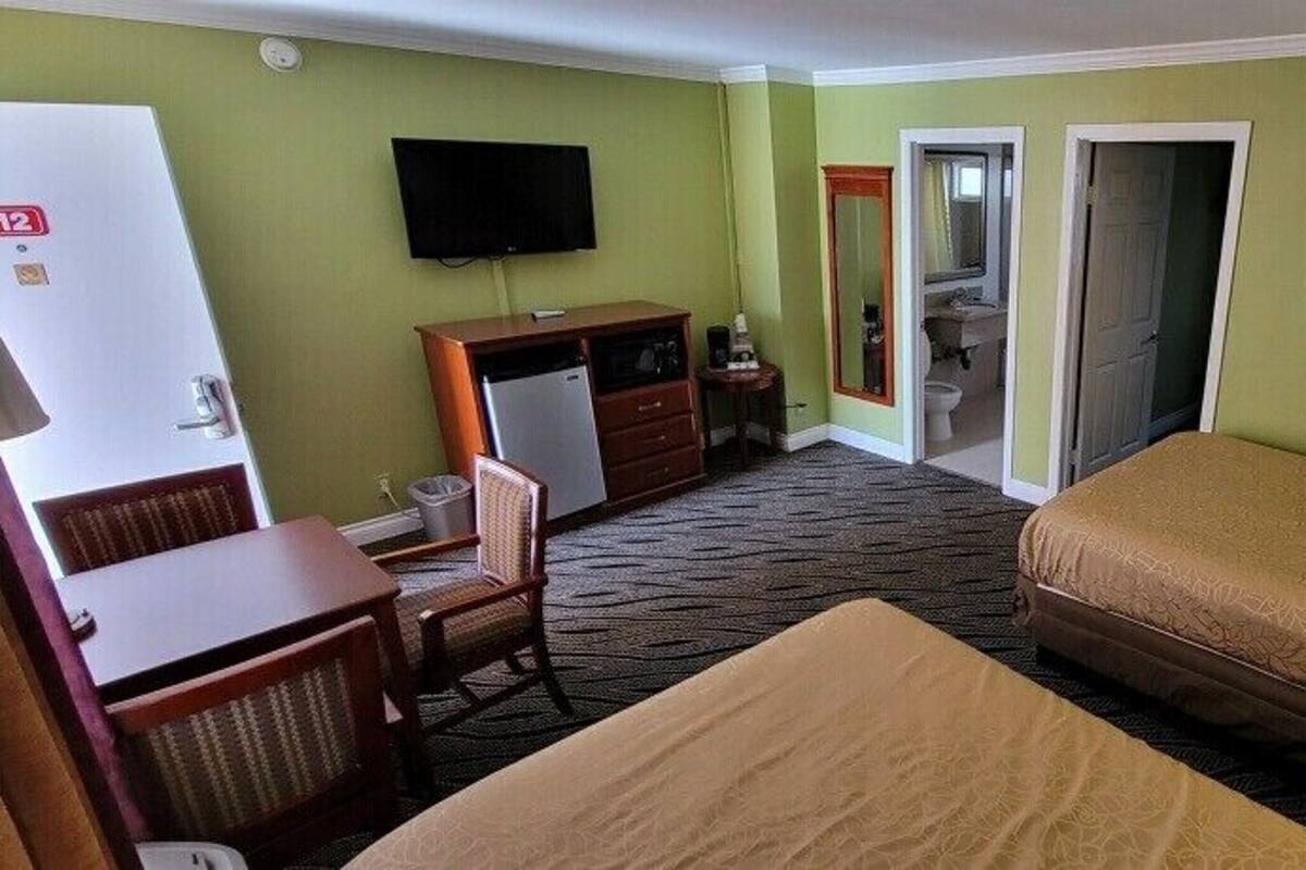 Habitación de hotel con cama, escritorio, silla, televisor y baño visible a través de una puerta abierta.