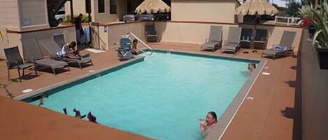 Une piscine sur le toit, agrémentée de chaises longues et de parasols, entourée d’un immeuble doté de balcons et d’un escalier.