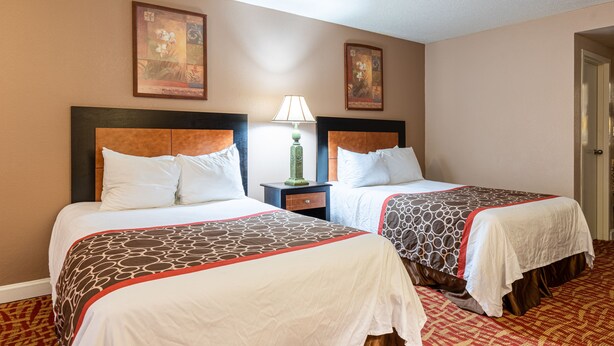 A hotel room with two beds, a nightstand with a lamp, and two framed pictures on the wall.