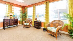 A room with two wicker chairs, a small cabinet with drawers, a lamp, and a large window with curtains.