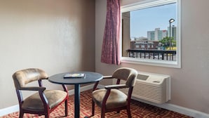 A hotel room with a small table and two chairs, a window with a view of the city, and a radiator.