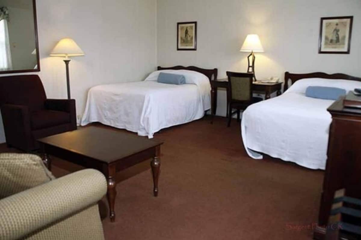 Habitación de hotel con dos camas individuales, un escritorio, una silla, una mesita y dos lámparas.