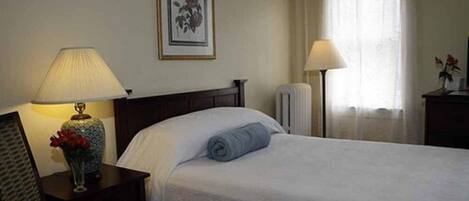 Een hotelkamer met een bed, een nachtkastje met lamp, een lijst met foto aan de muur, en een raam met gordijnen.