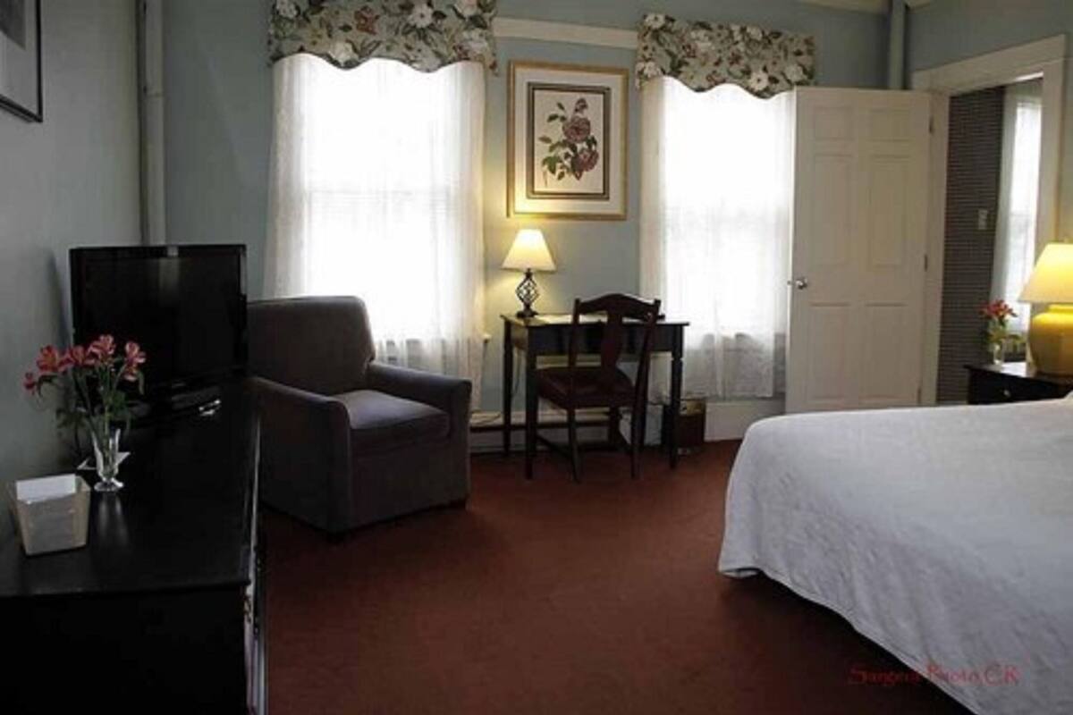 Una habitación de hotel con cama, escritorio, silla, televisor y lámpara.