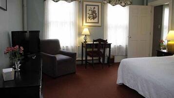 A hotel room with a bed, a desk with a chair, a television, and a lamp.