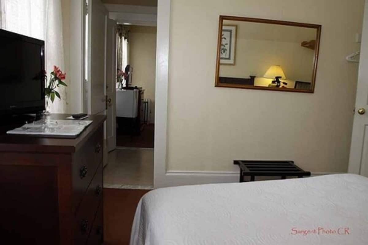 Una habitación de hotel con cama, televisión, escritorio con lámpara y espejo en la pared.