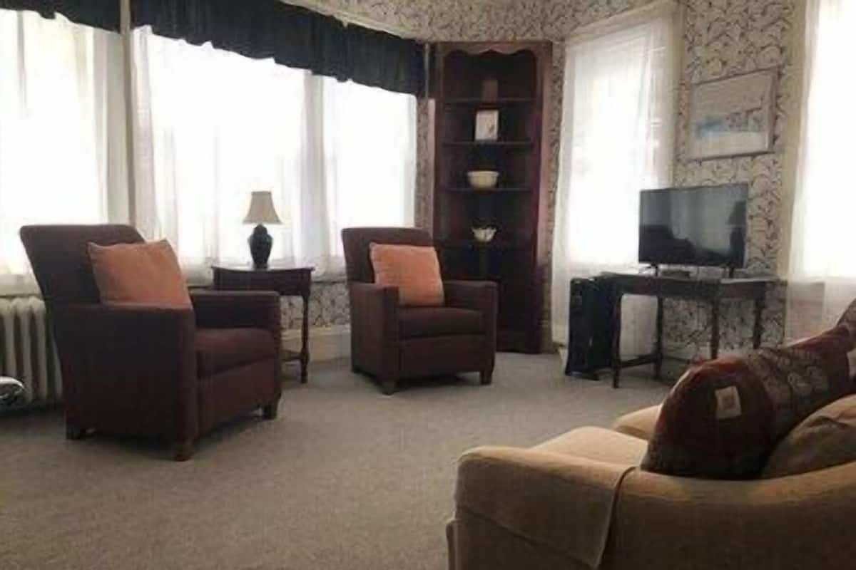 Una sala de estar con dos sillones, un sofá, un televisor y una estantería.