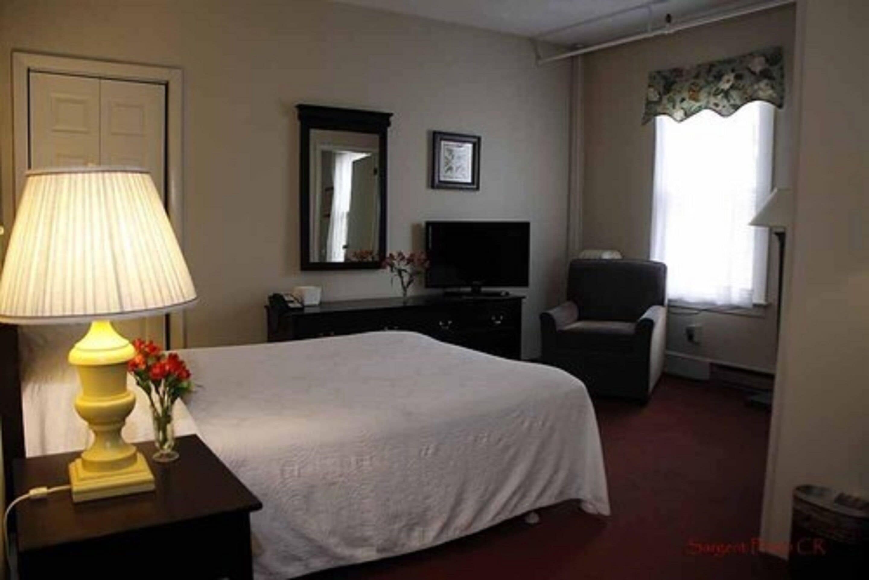 A hotel room with a bed, a TV, a chair, a lamp, and a mirror.