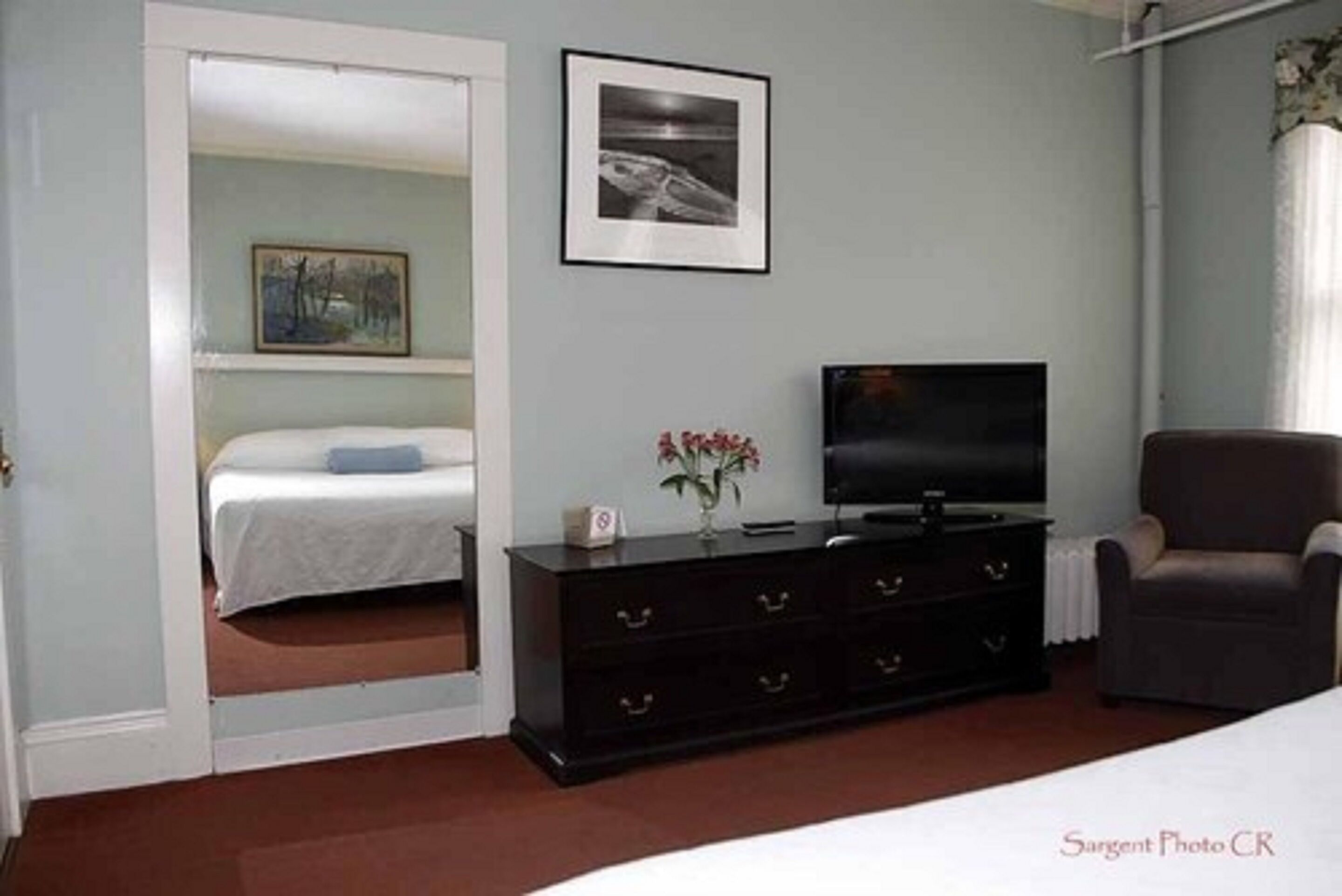 Une chambre à coucher avec un lit, une commode, un téléviseur et une chaise.