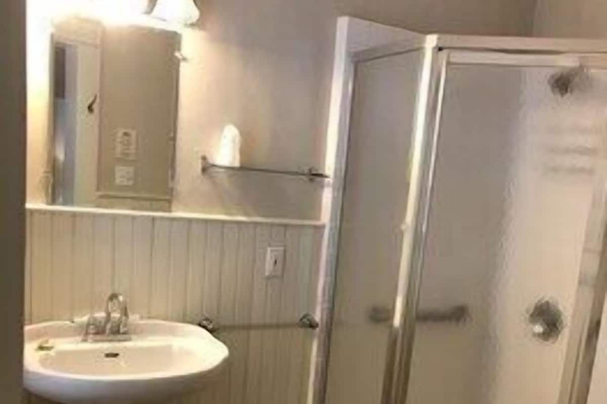 Un baño con lavamanos pedestal, espejo y cabina de ducha con mampara de vidrio.