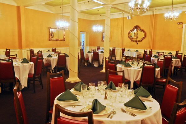 A formal dining room with multiple tables, red chairs, and chandeliers. - Hotel Coolidge (White River Junction)
