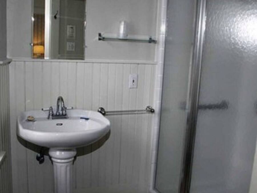 A bathroom with a pedestal sink, a mirror above it, a towel rack, and a shower with a glass door.