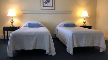 Two single beds with matching pillows and bedside tables, set against a simple, clean backdrop.