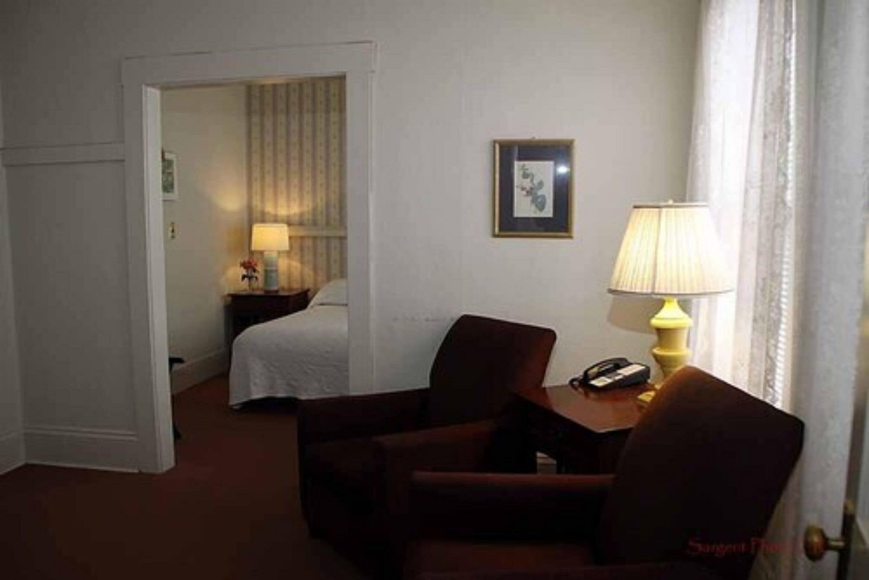 A hotel room with a bed, a chair, a nightstand with a lamp, and a framed picture on the wall.