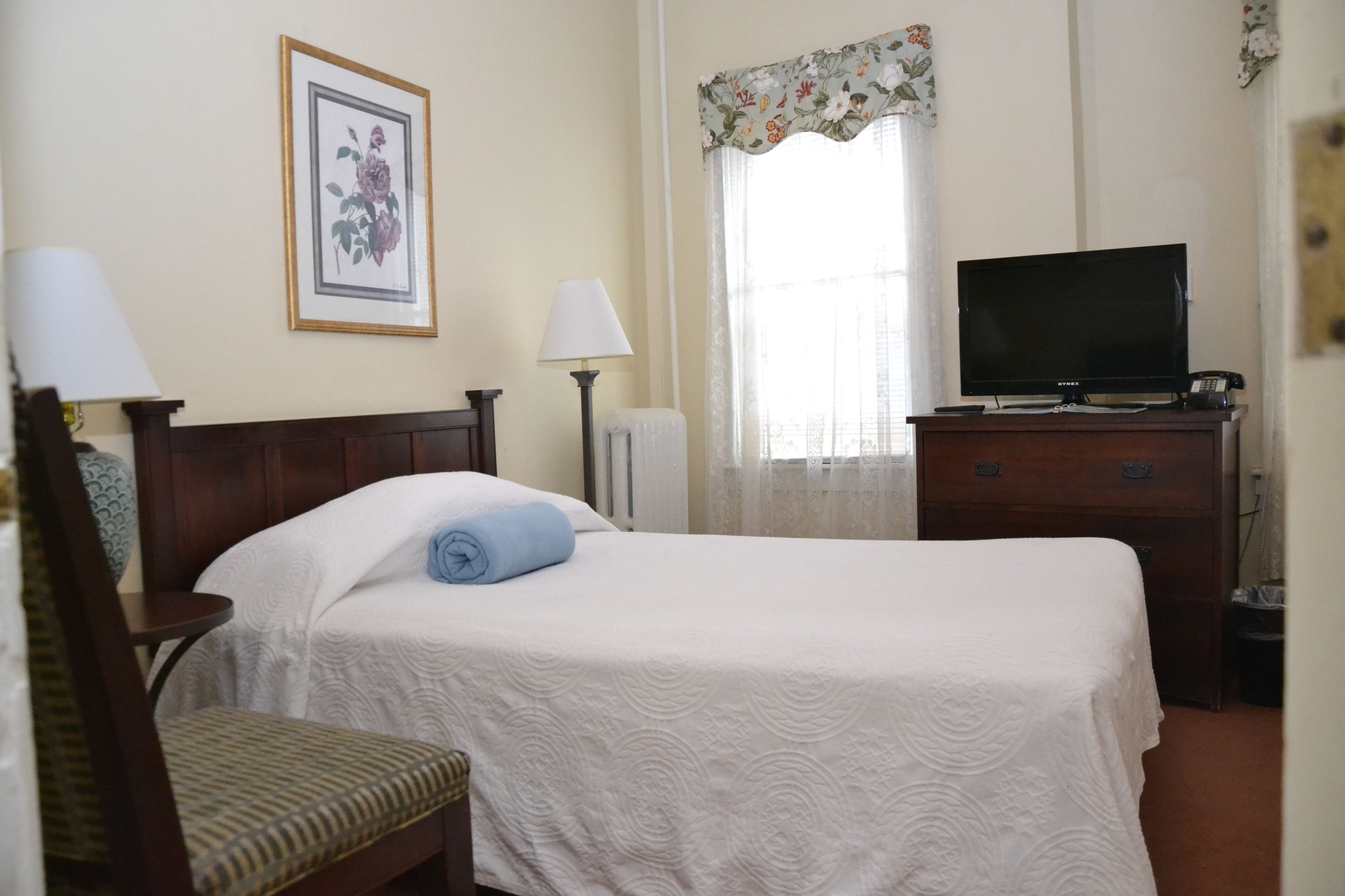 Une chambre d’hôtel avec un lit, une chaise, un bureau avec une télévision et un tableau encadré au mur.