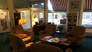Una sala de estar acogedora con sillones cómodos, una mesa de centro con libros, una lámpara y vistas a la calle.