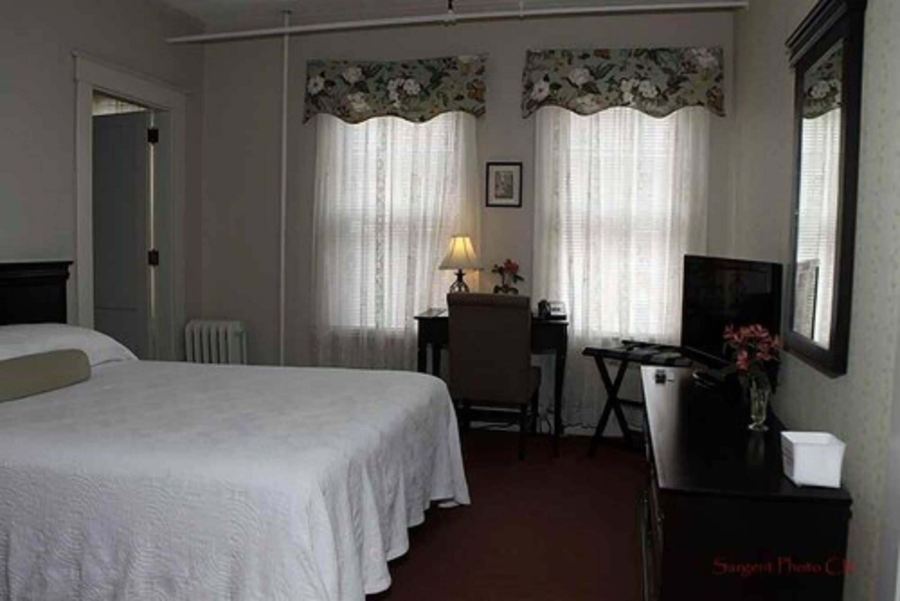 Una habitación de hotel con cama, escritorio con silla, televisor y radiador.