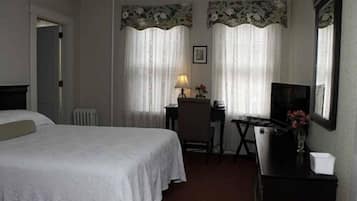Una habitación de hotel con cama, escritorio con silla, televisor y radiador.