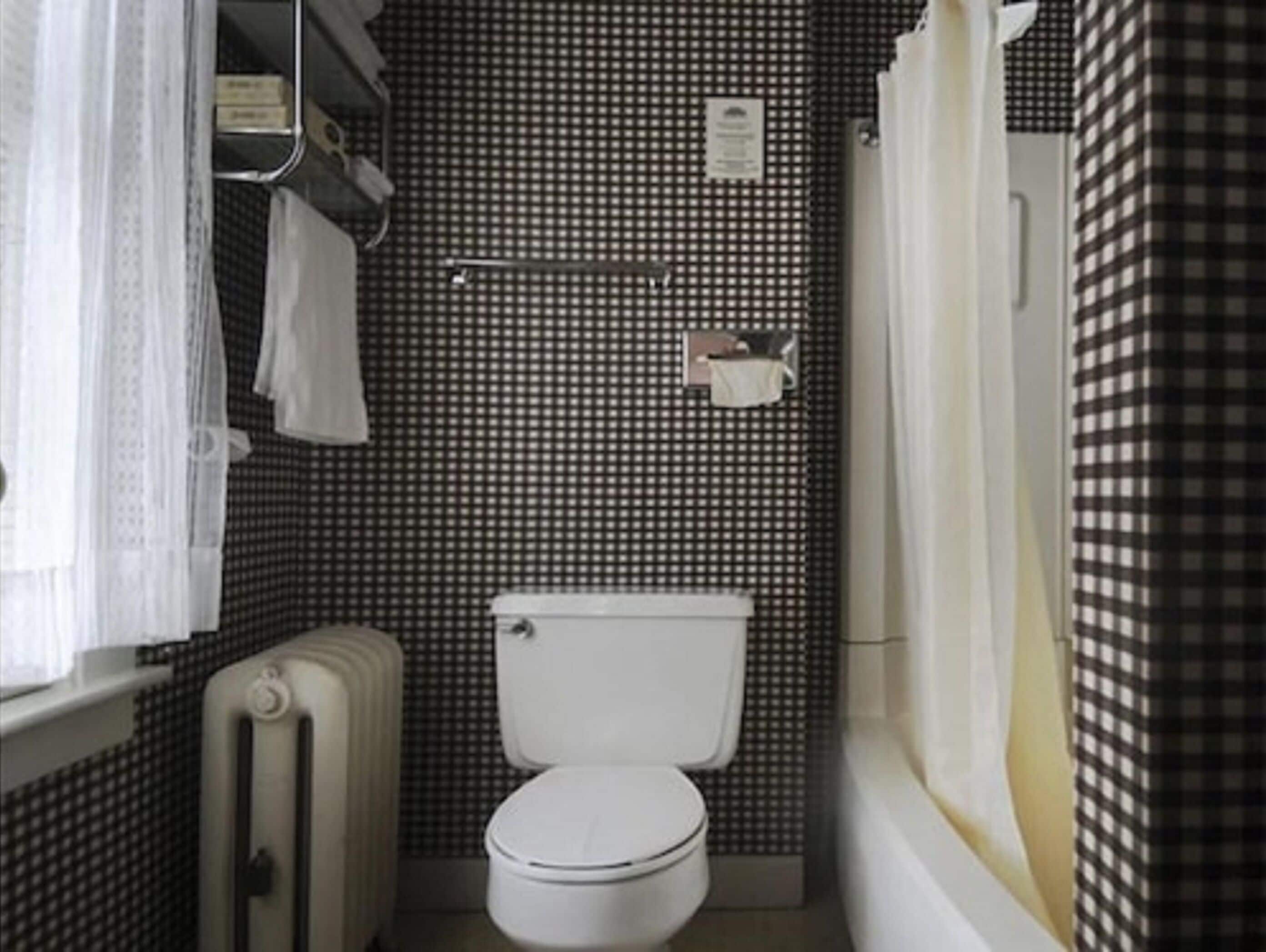 A small bathroom with a white toilet, a radiator, and a checkered wall.