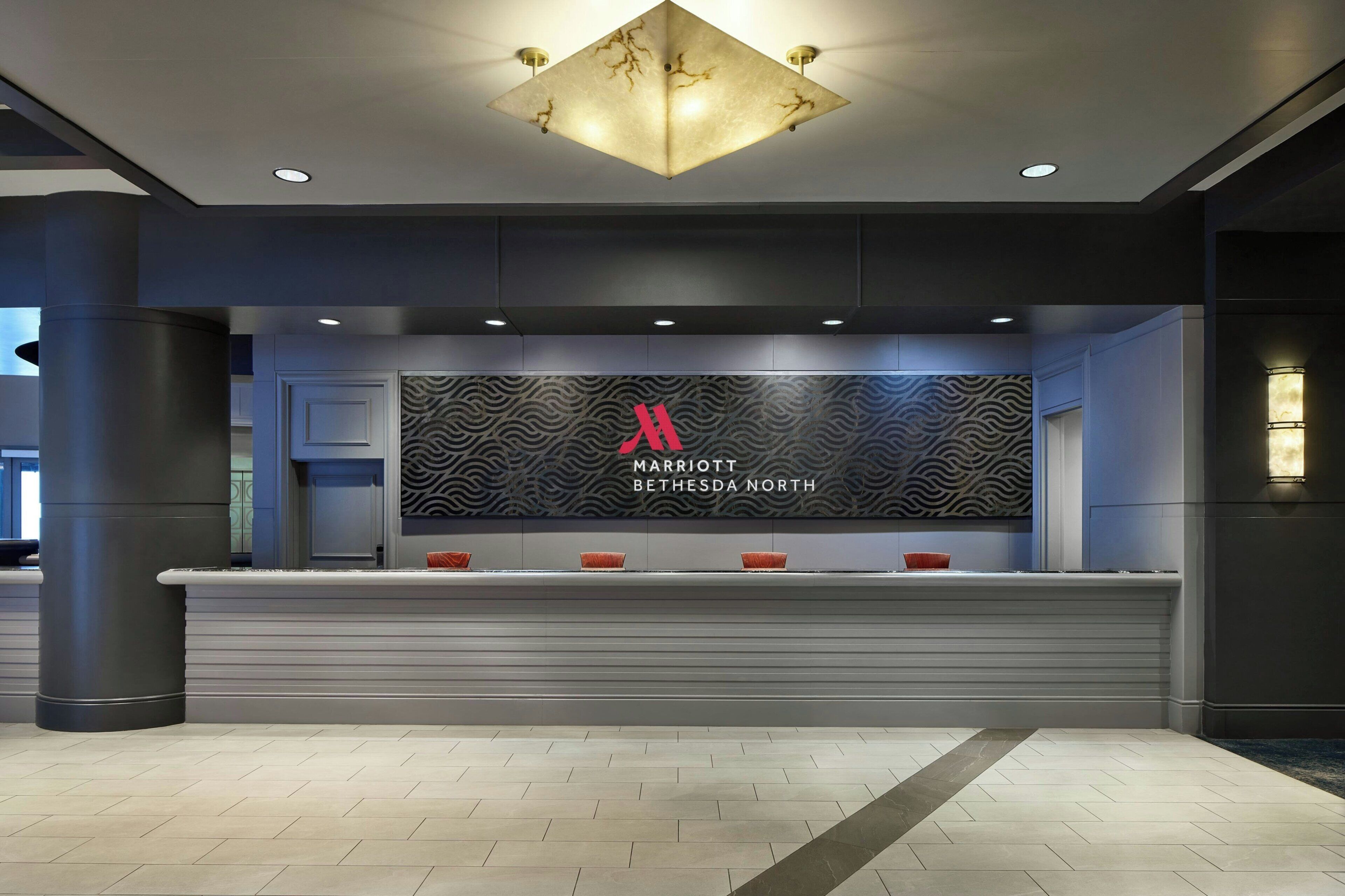 A reception desk with a large logo, a modern chandelier, and a patterned wall.