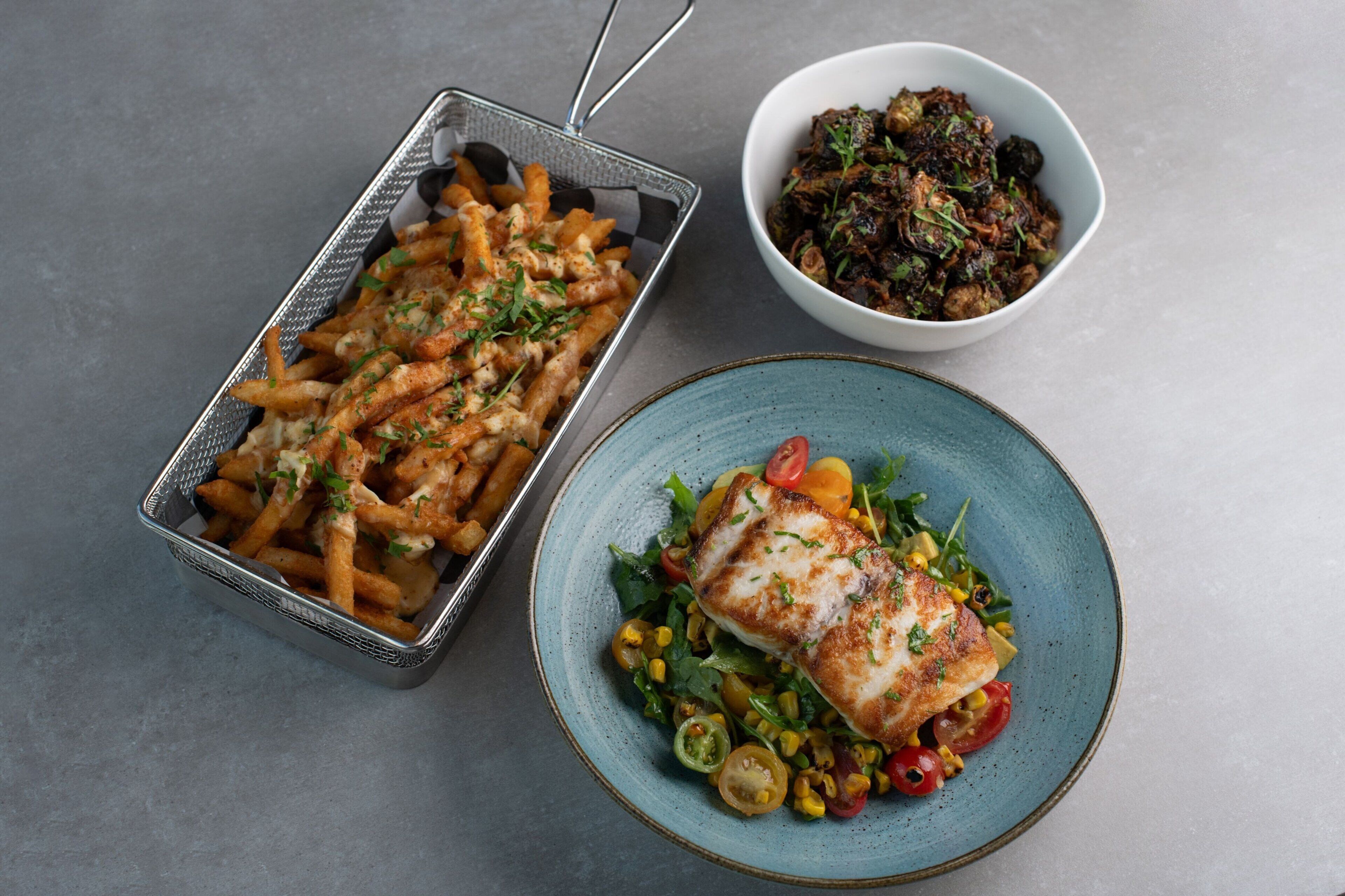 A meal consisting of fries, a bowl of salad, and a plate with a fish fillet.
