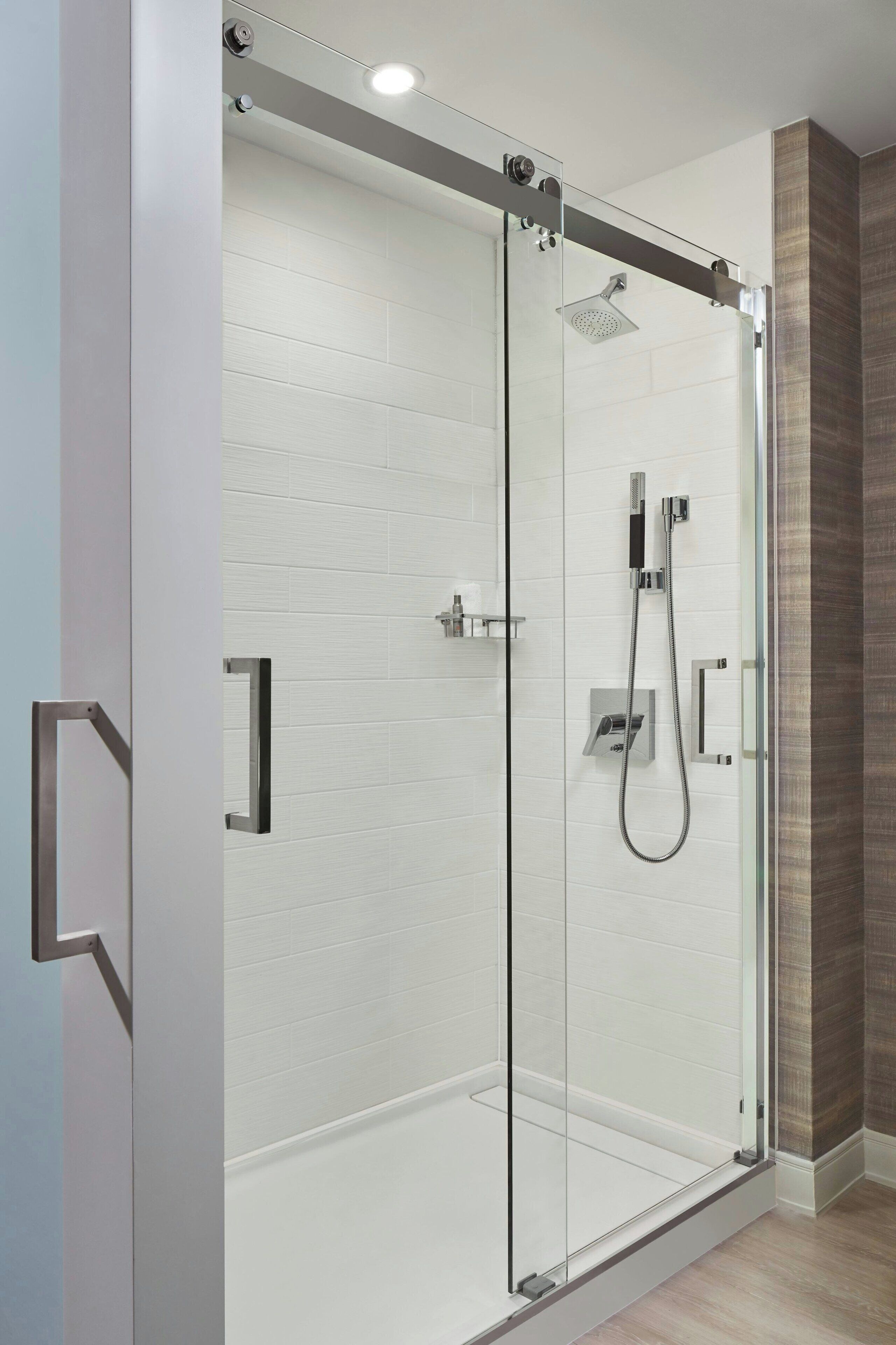 Un box de ducha moderno con puerta de cristal, cabezal de ducha de mano y panel de control en la pared.