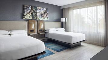 Habitación de hotel con dos camas, un ventanal con cortinas translúcidas, una obra de arte colgada en la pared y una mesita de noche con lámparas.