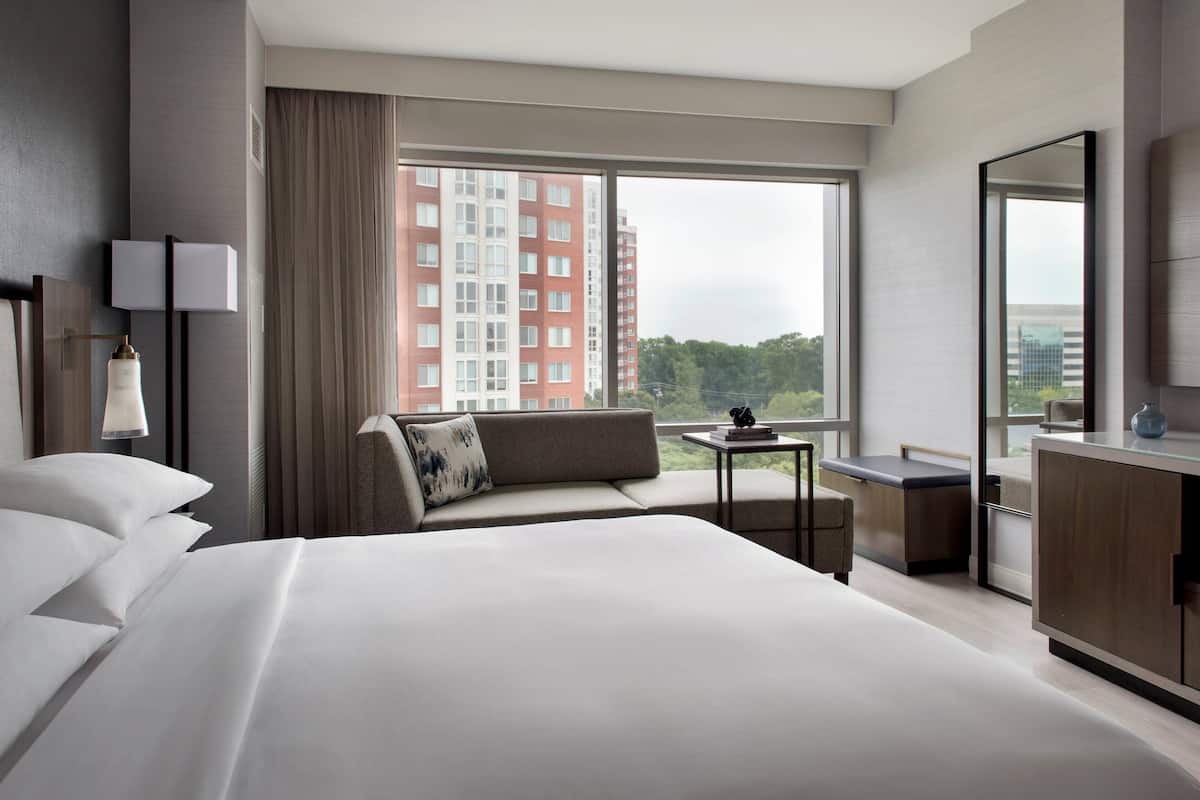 Une chambre d’hôtel moderne avec un grand lit, un canapé, une petite table et une vue sur le paysage urbain.