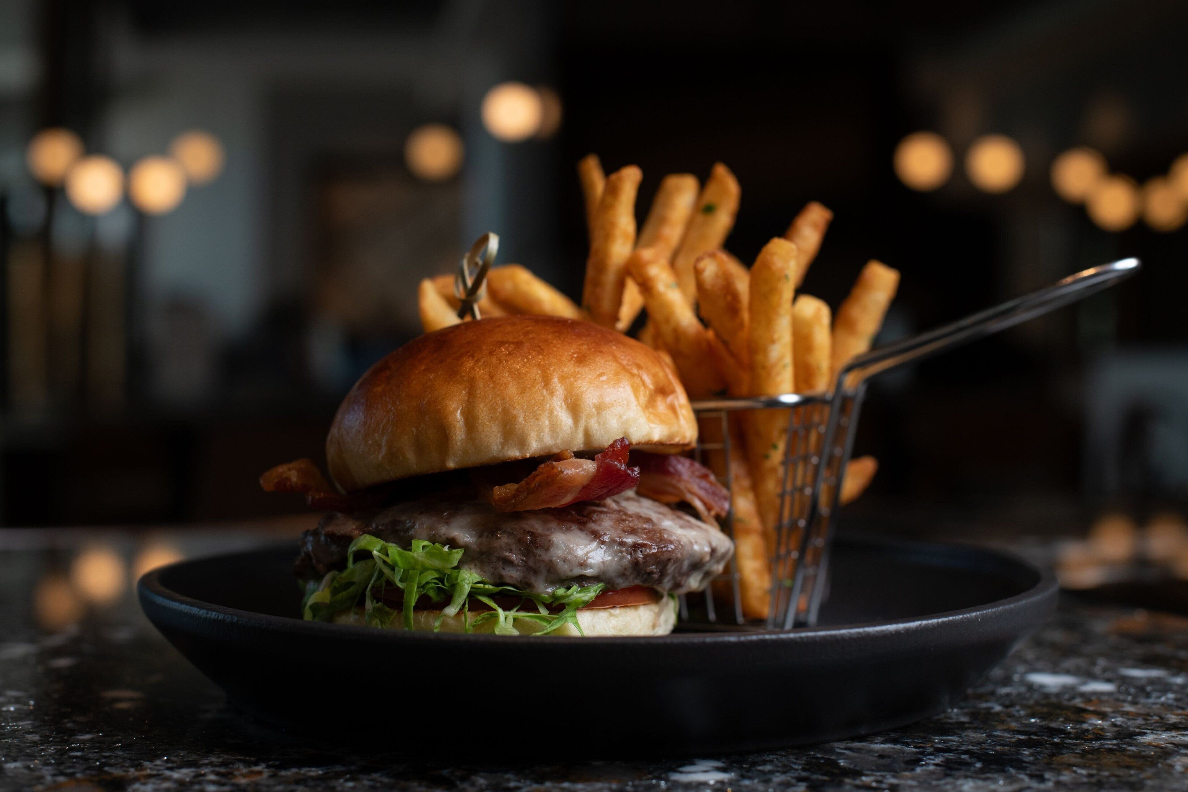 En burger med pommes frites i en sort skål på en marmor bordplade.