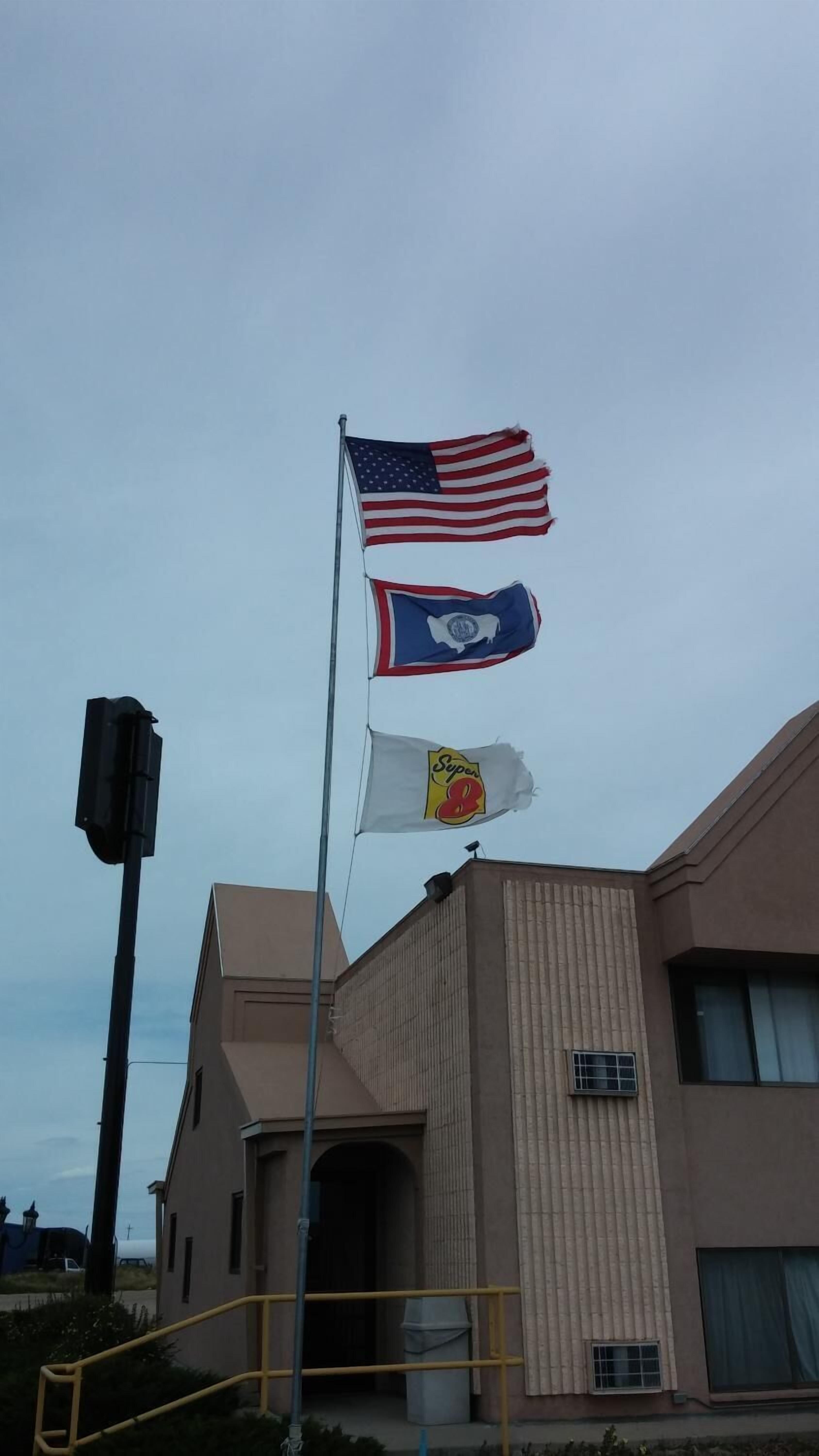 A building with a beige facade and a flagpole with three flags.