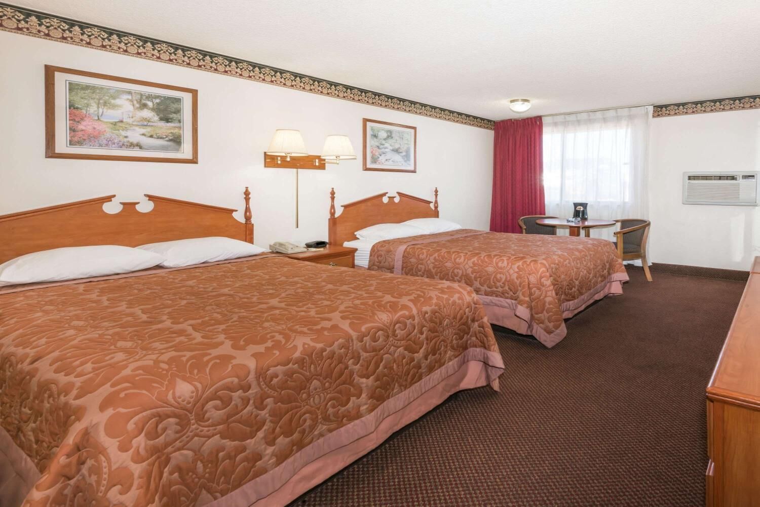 A hotel room with two beds, a desk, a chair, a lamp, and a window with curtains.