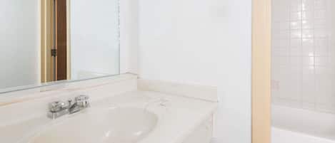 Un baño con lavamanos blanco, espejo y bañera.
