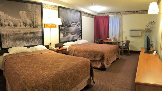 Habitación de hotel con dos camas, un escritorio, una silla, una lámpara y un cuadro grande en la pared.